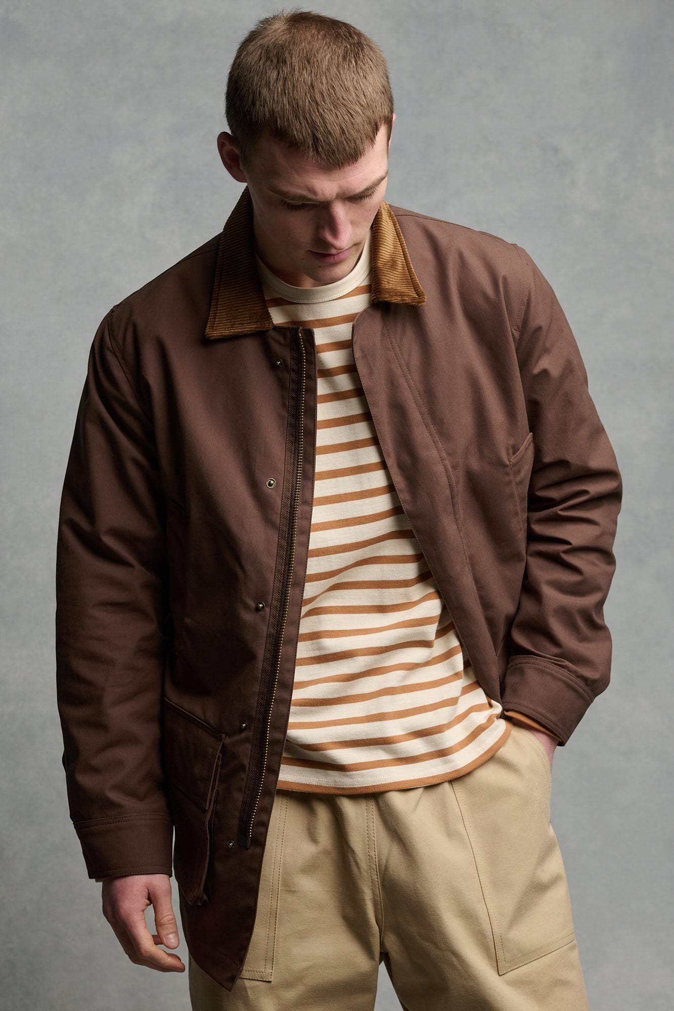 Thigh up image of male wearing men's barn jacket in brown unzipped over Breton in ecru cinnamon paired with cameraman pant in putty