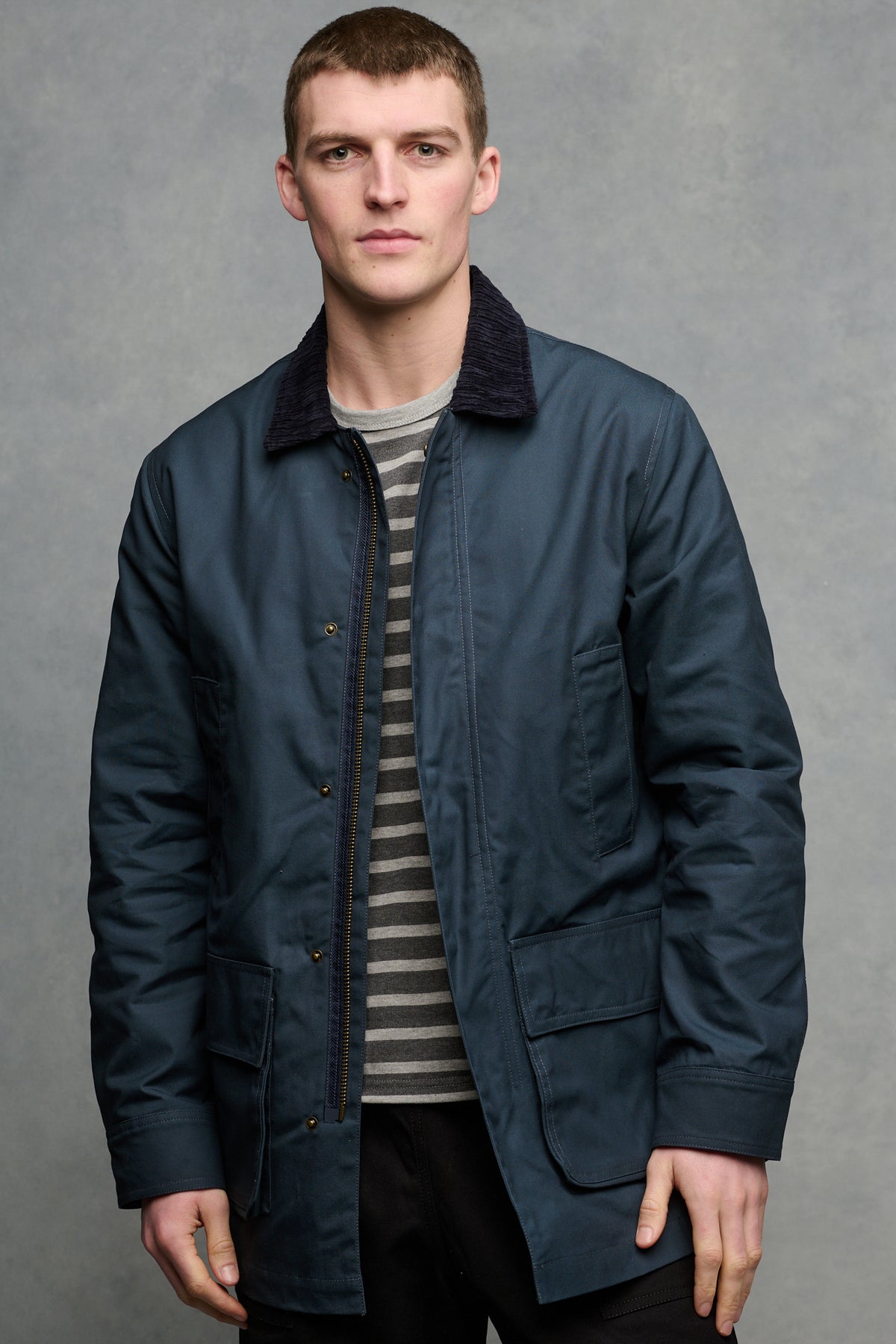 Thigh up image of brunet male wearing barn jacket in navy unzipped open over Breton in charcoal and grey marl