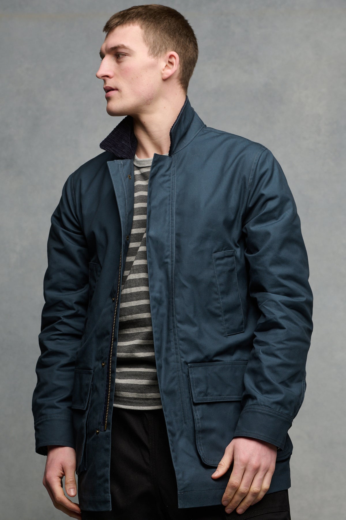 Thigh up image of the front of male wearing barn jacket in navy unzipped over Breton in charcoal and grey