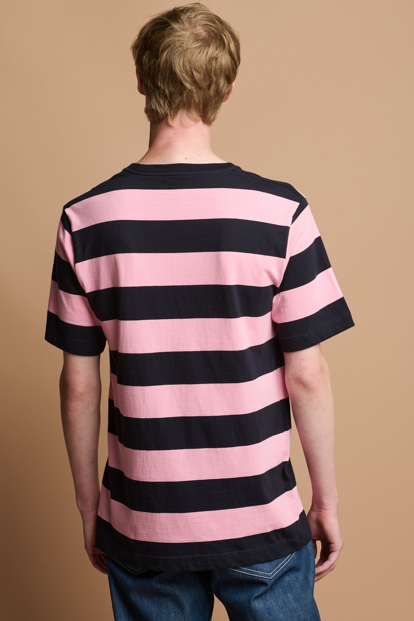 Thigh up image of smiley male wearing wide stripe short sleeve t shirt in navy blue and pink stripe