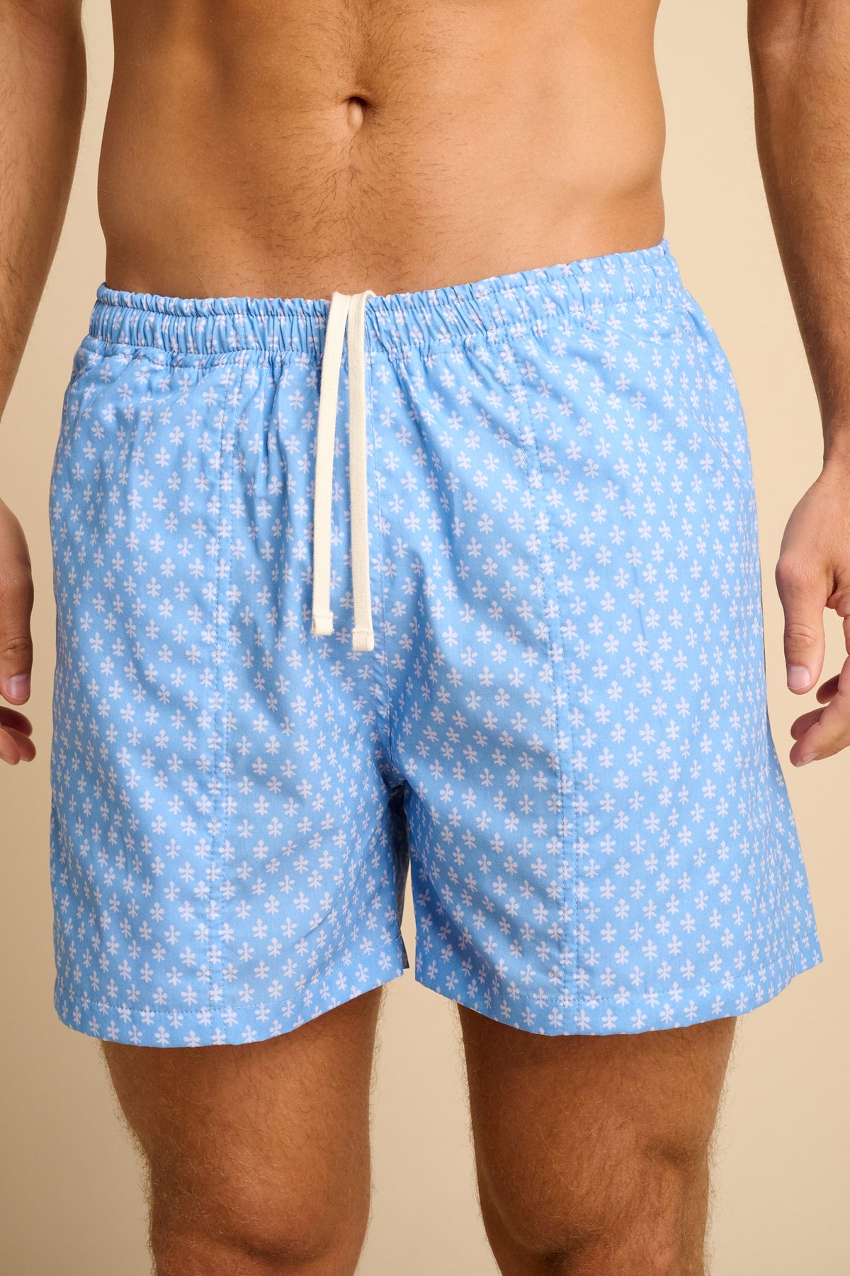 Man wearing light blue print swim shorts on a beige background.