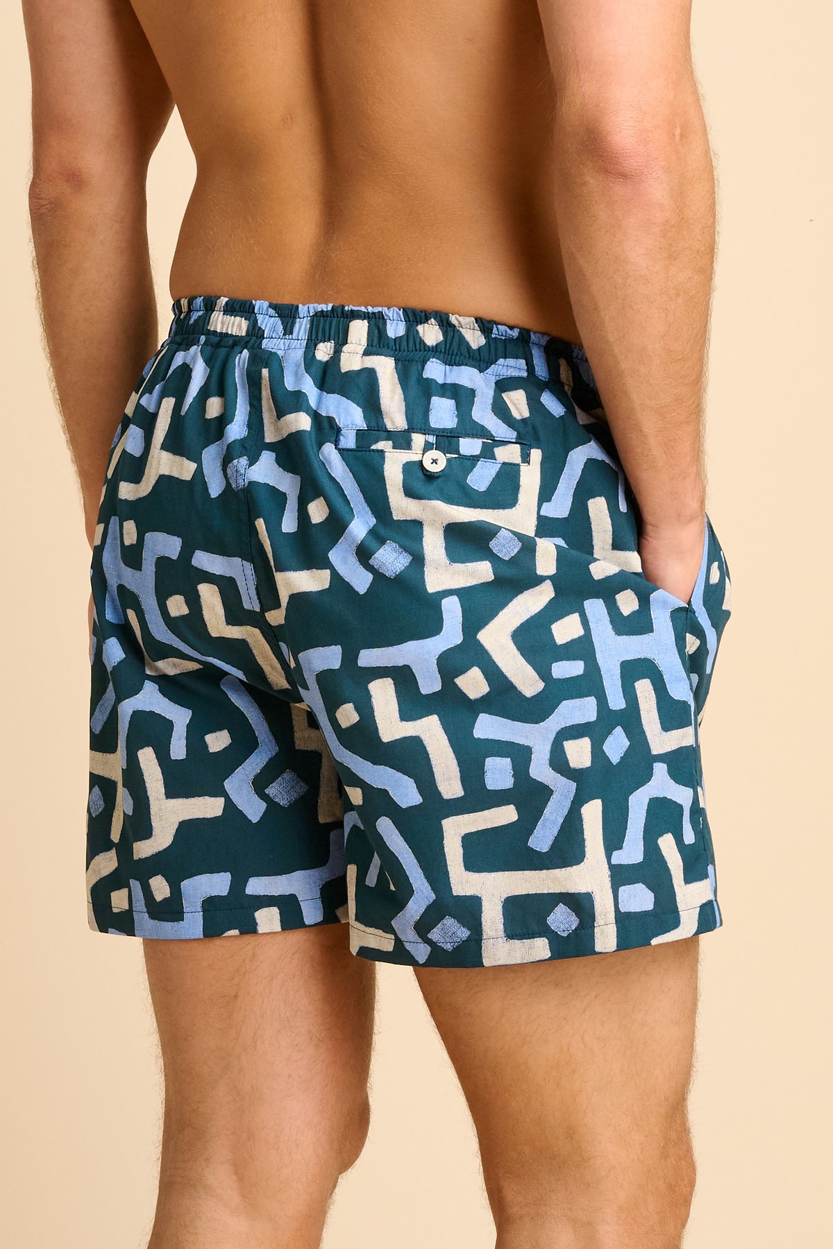 Man wearing blue swim shorts with a geometric pattern on a beige background