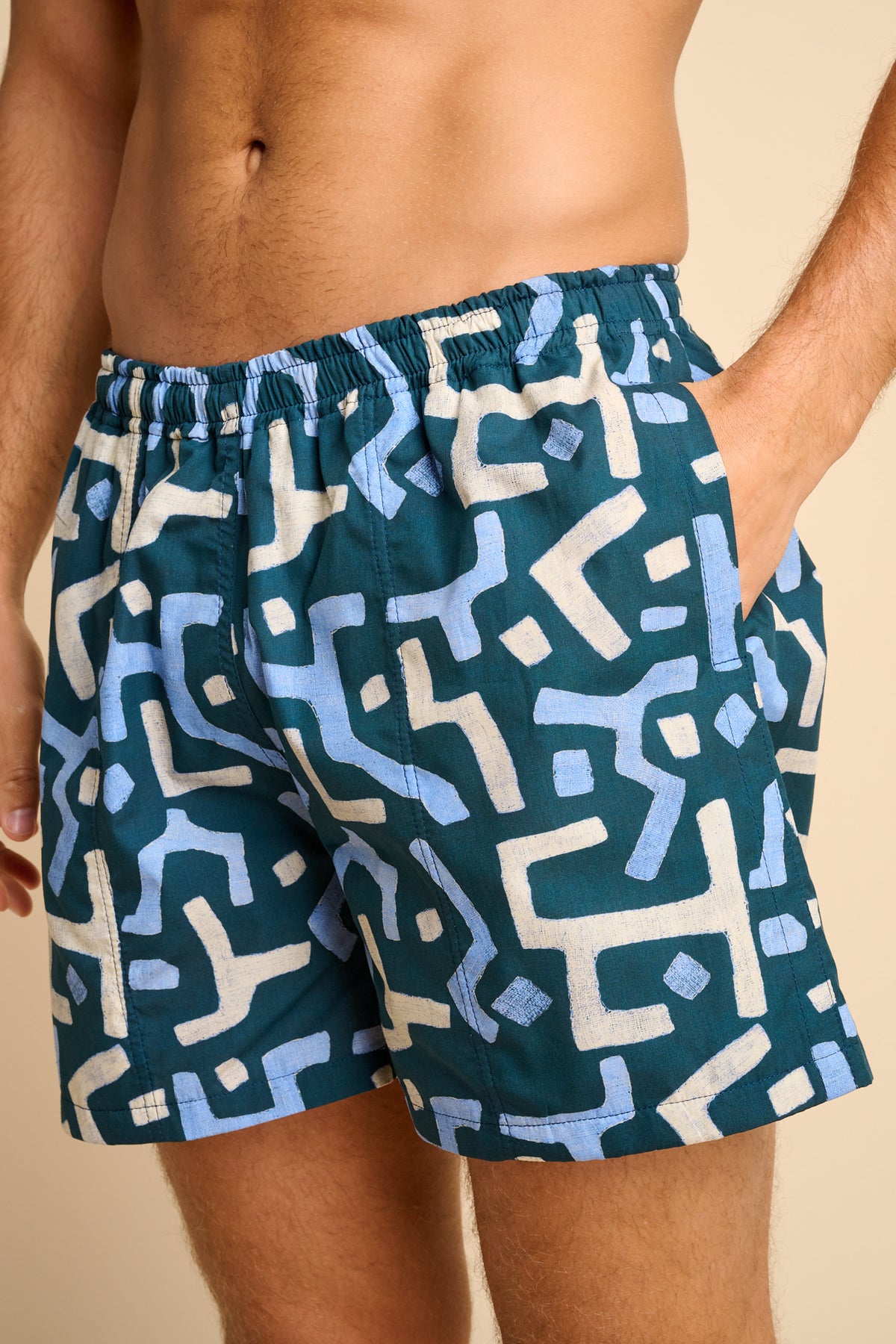 Man wearing blue swim shorts with a geometric pattern on a beige background
