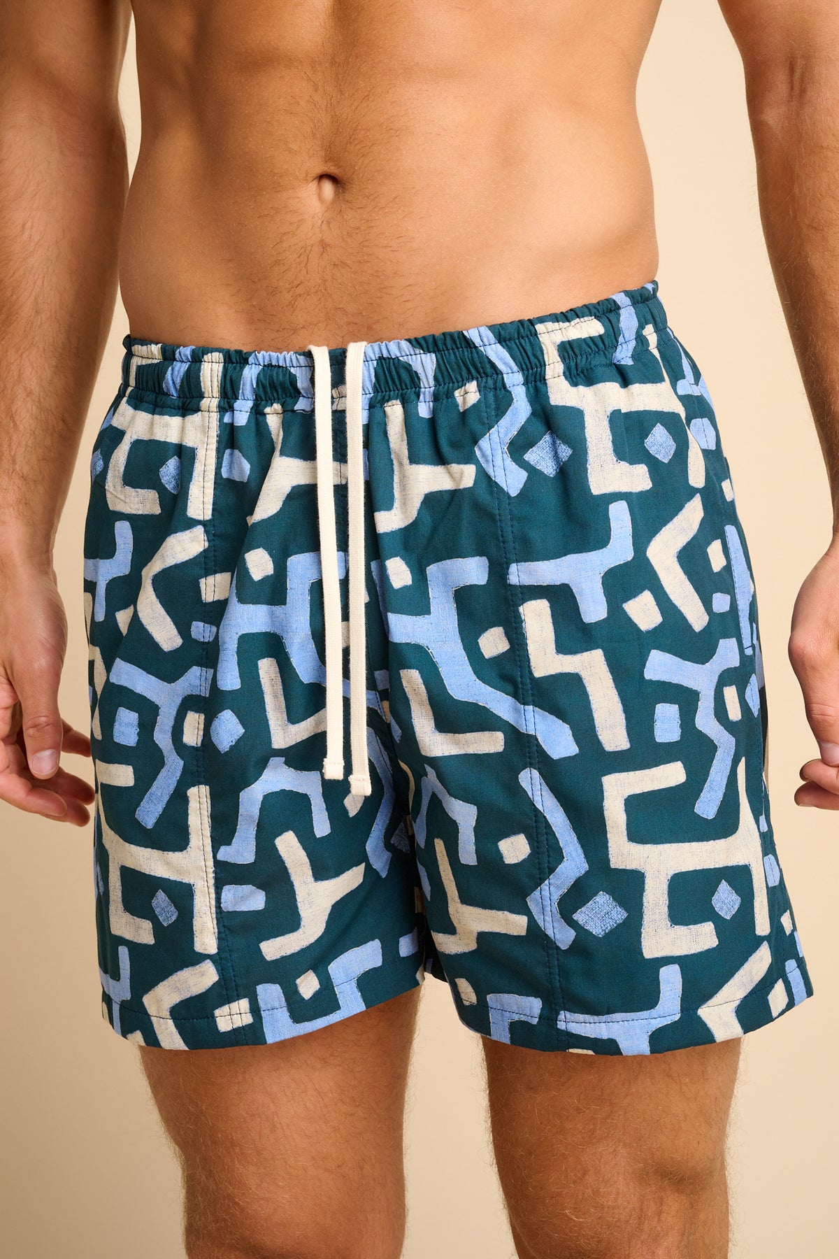 Man wearing blue swim shorts with a geometric pattern on a beige background