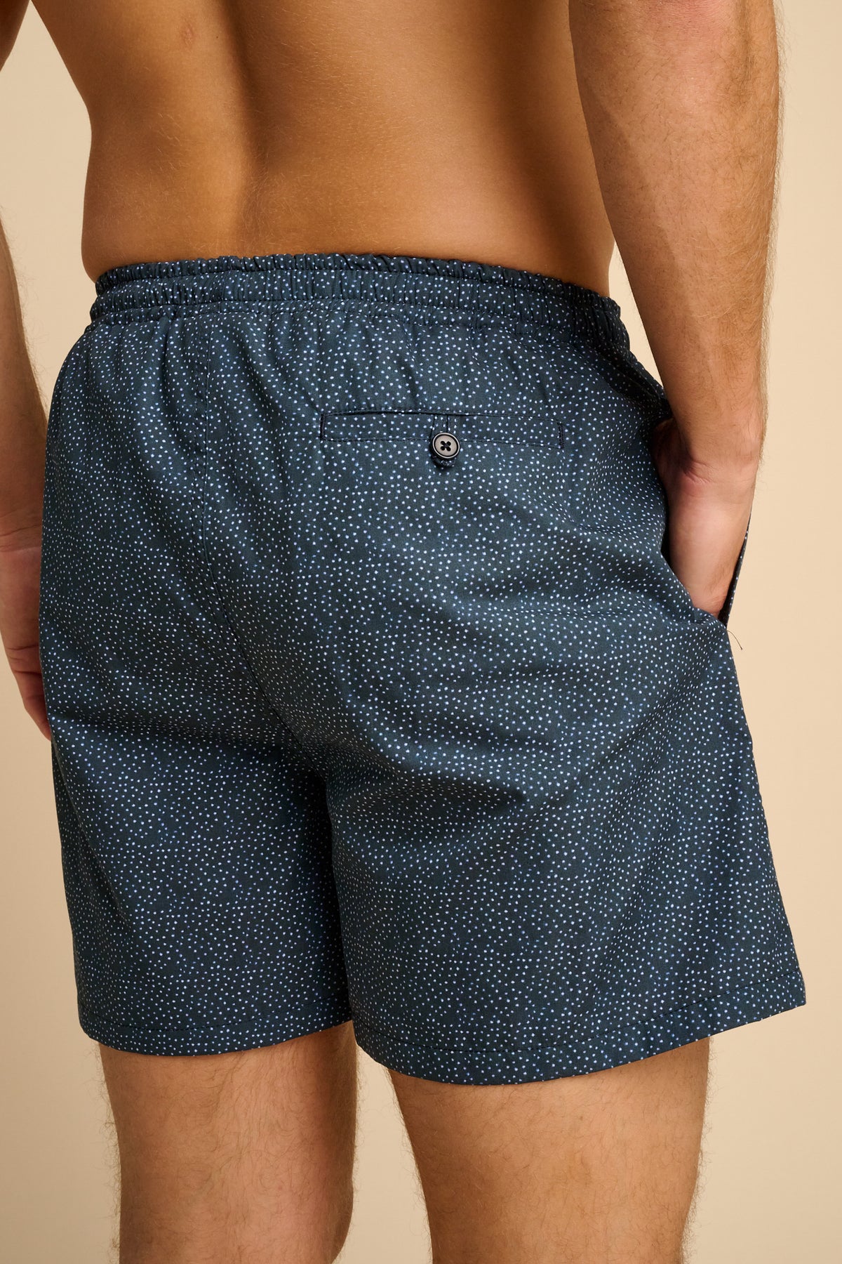 Man wearing navy blue polka dot swim shorts against a beige background.