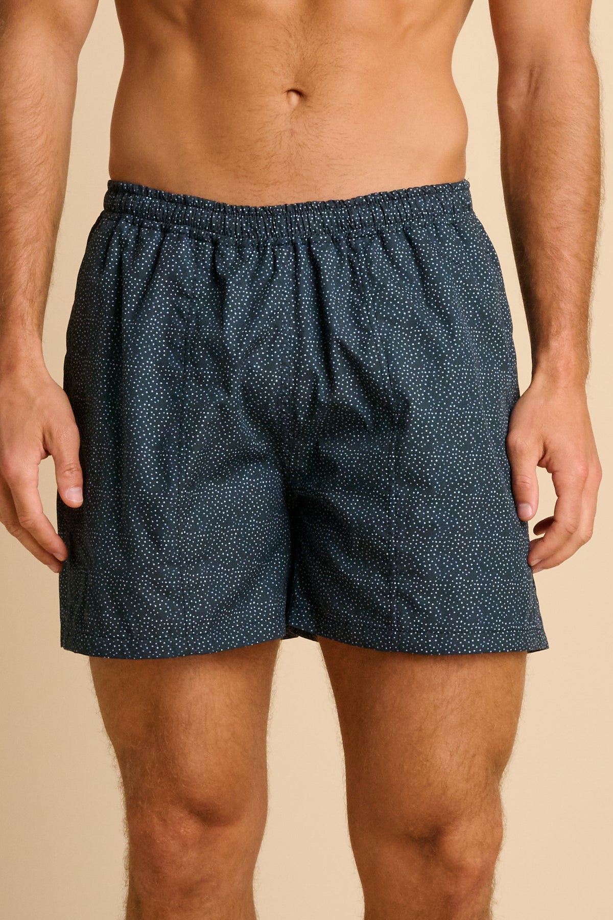 Man wearing navy polka dot swim shorts against a beige background.