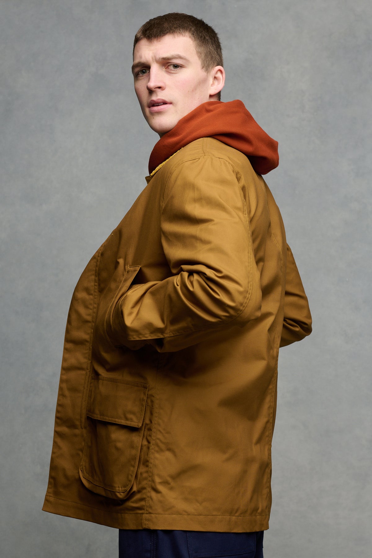 The side of brunet male wearing car coat in dark tan with hand in front pockets.
