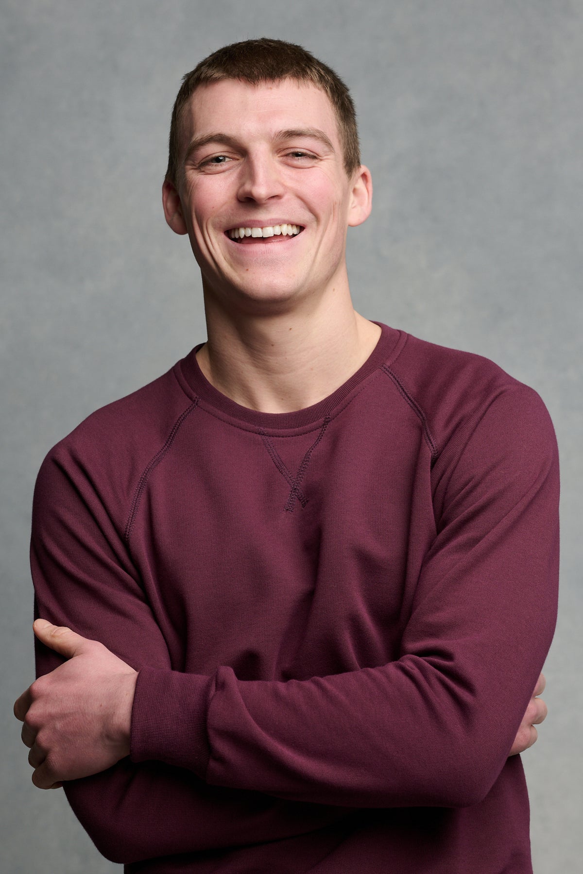 Waist up image of the front of smiley male wearing raglan sweatshirt in plum