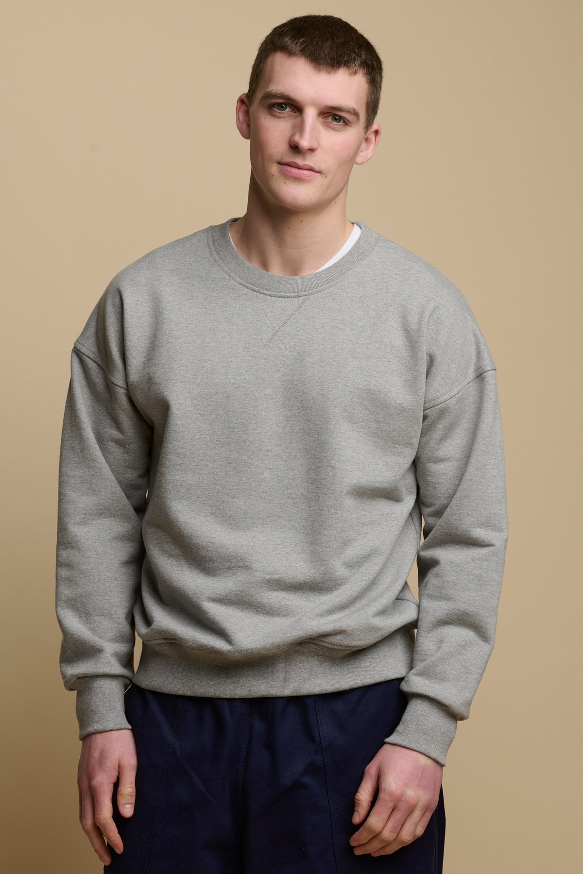 Thigh up front of brunet male wearing men's heritage drop shoulder sweatshirt in grey, worn over crew neck white t shirt paired with cameraman pants in navy
