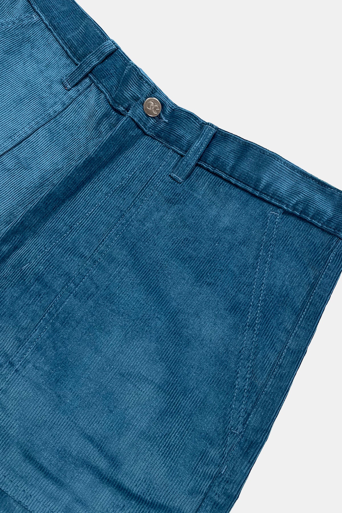 Close-up of blue corduroy trousers showing the waistband, belt loops, and button closure against a white background.