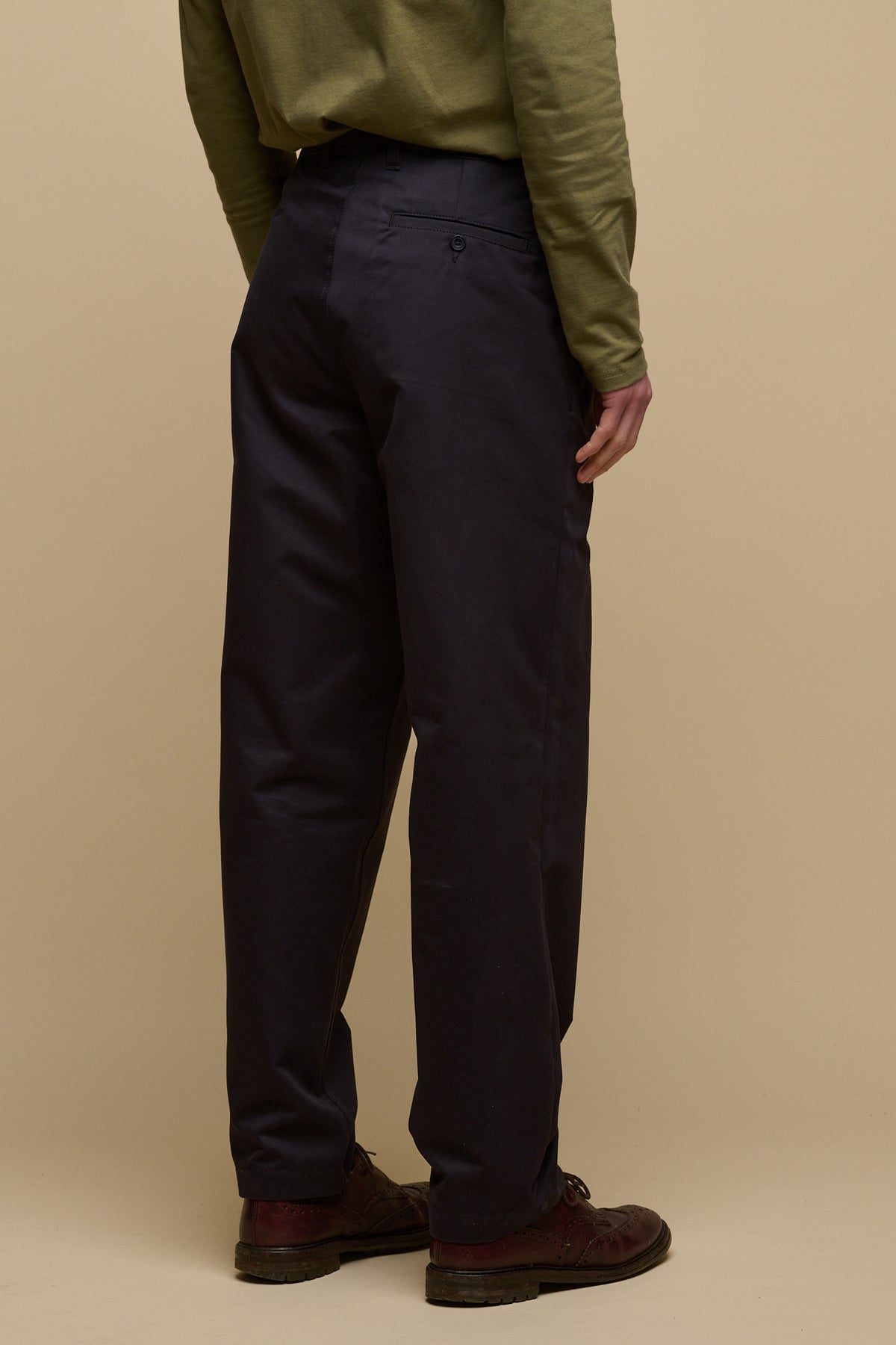 Waist down image of the back of male wearing pleated chino in navy with back pocket with button fastening 