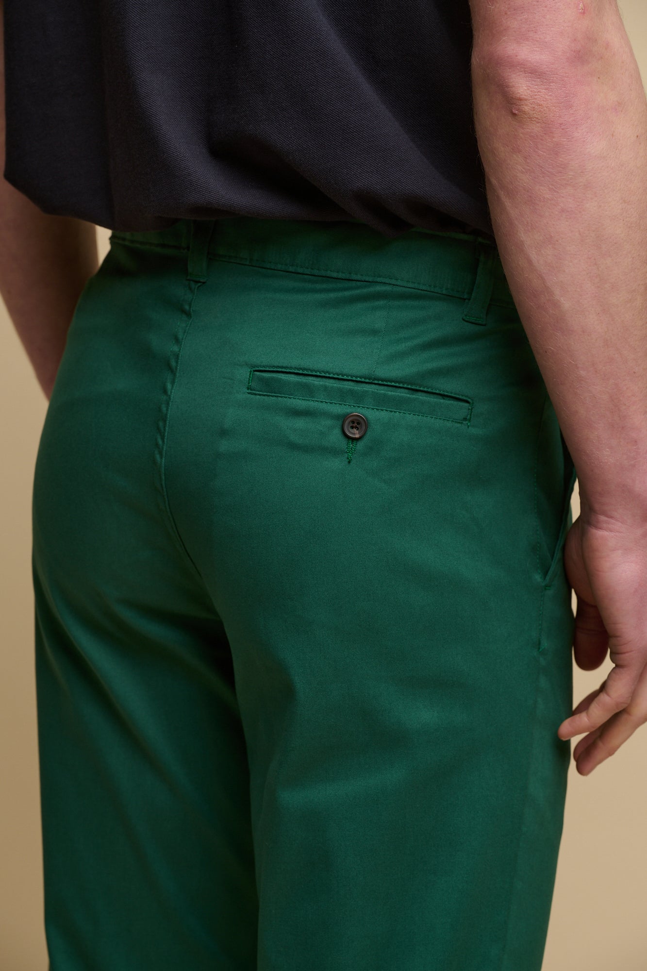 Full body image of brunet male wearing men's slim stretch chino in bottle green paired with short sleeve polo shirt in navy and sandals