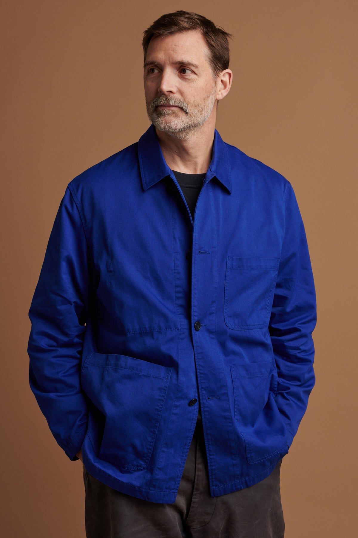 Thigh up of Patrick wearing chore jacket in royal blue over heritage sweatshirt in navy