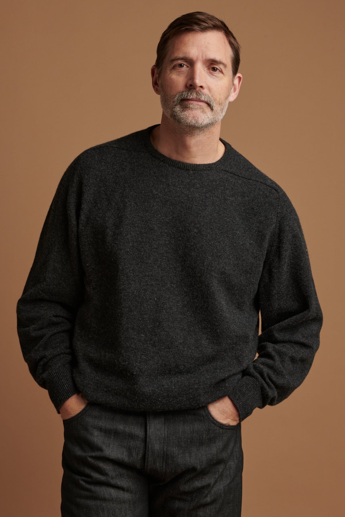 Patrick wearing lambswool saddle shoulder crew neck jumper in charcoal  paired with loose fit button fly Arran jean in black