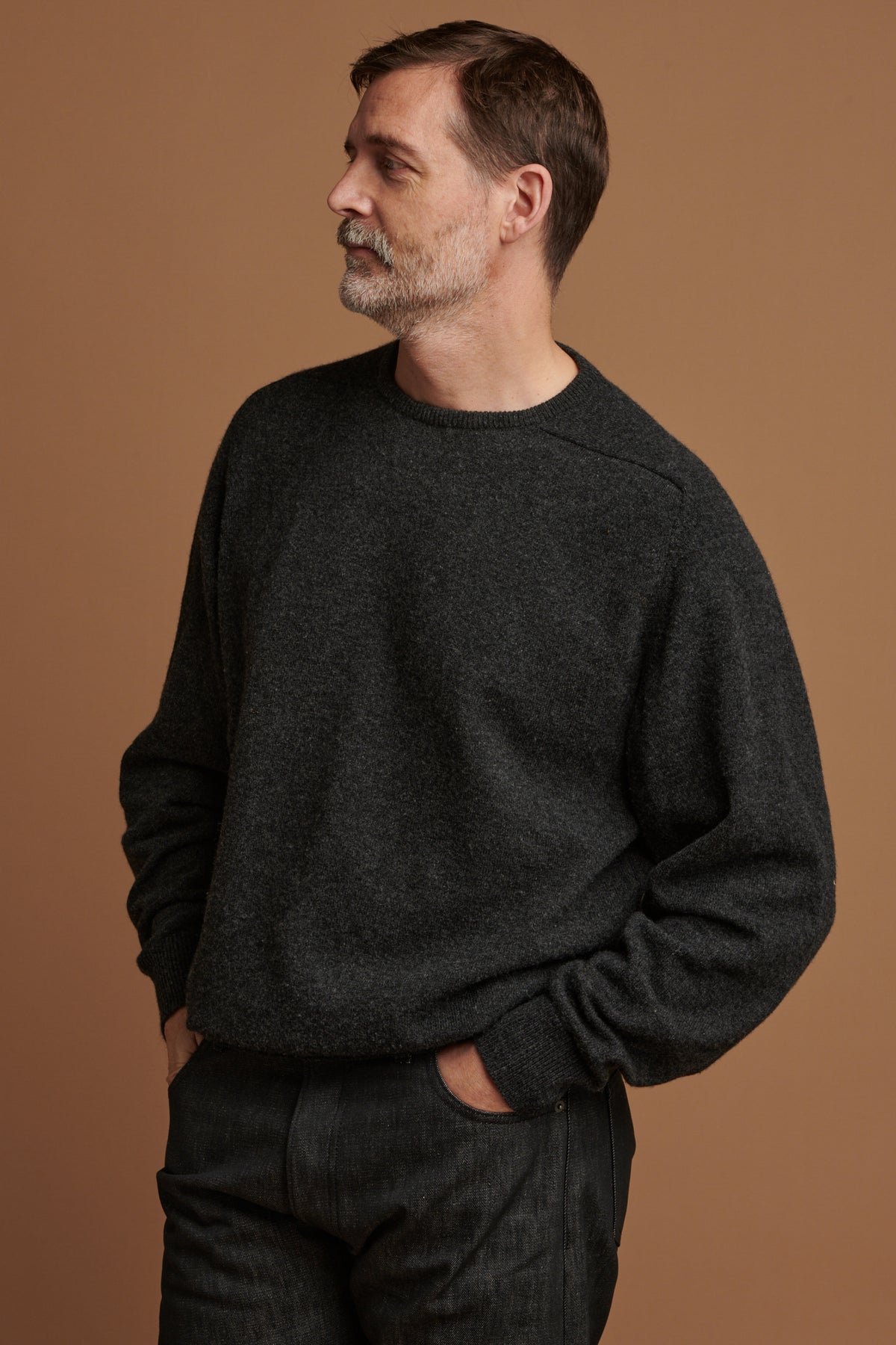 Patrick wearing lambswool saddle shoulder crew neck jumper in charcoal  paired with loose fit button fly Arran jean in black