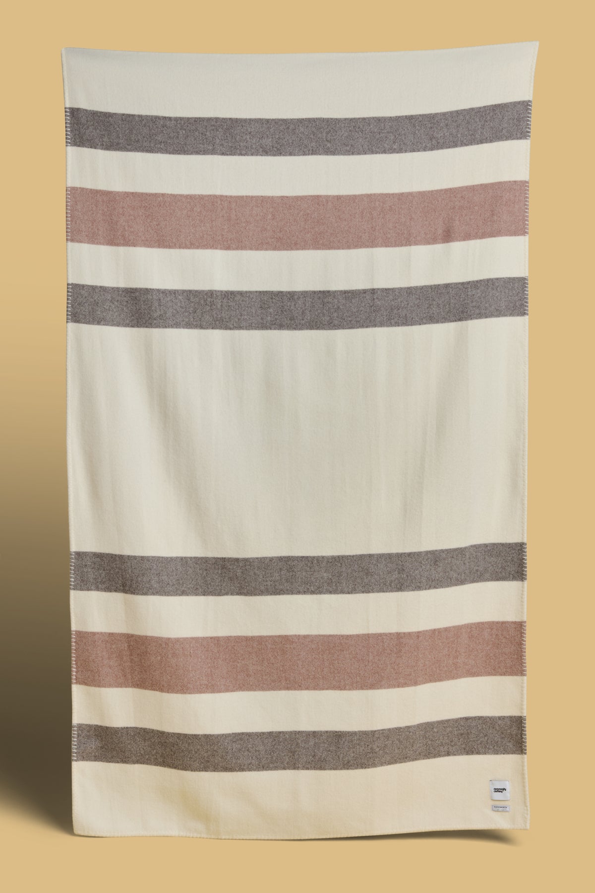 Blanket in ecru dark brown and tan stripe with Community Clothing woven logo in the bottom right hand corner.