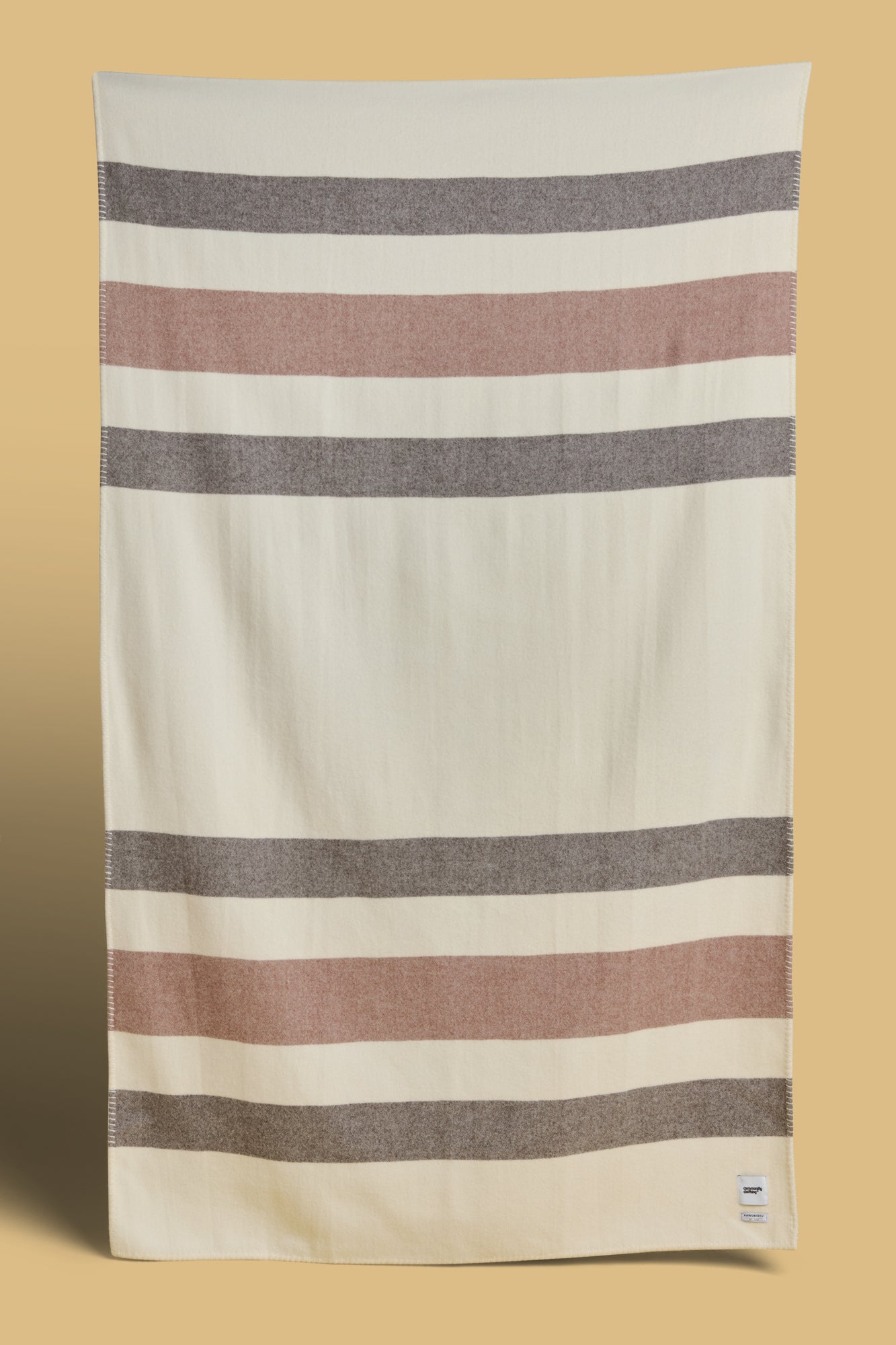 Blanket in ecru dark brown and tan stripe with Community Clothing woven logo in the bottom right hand corner.