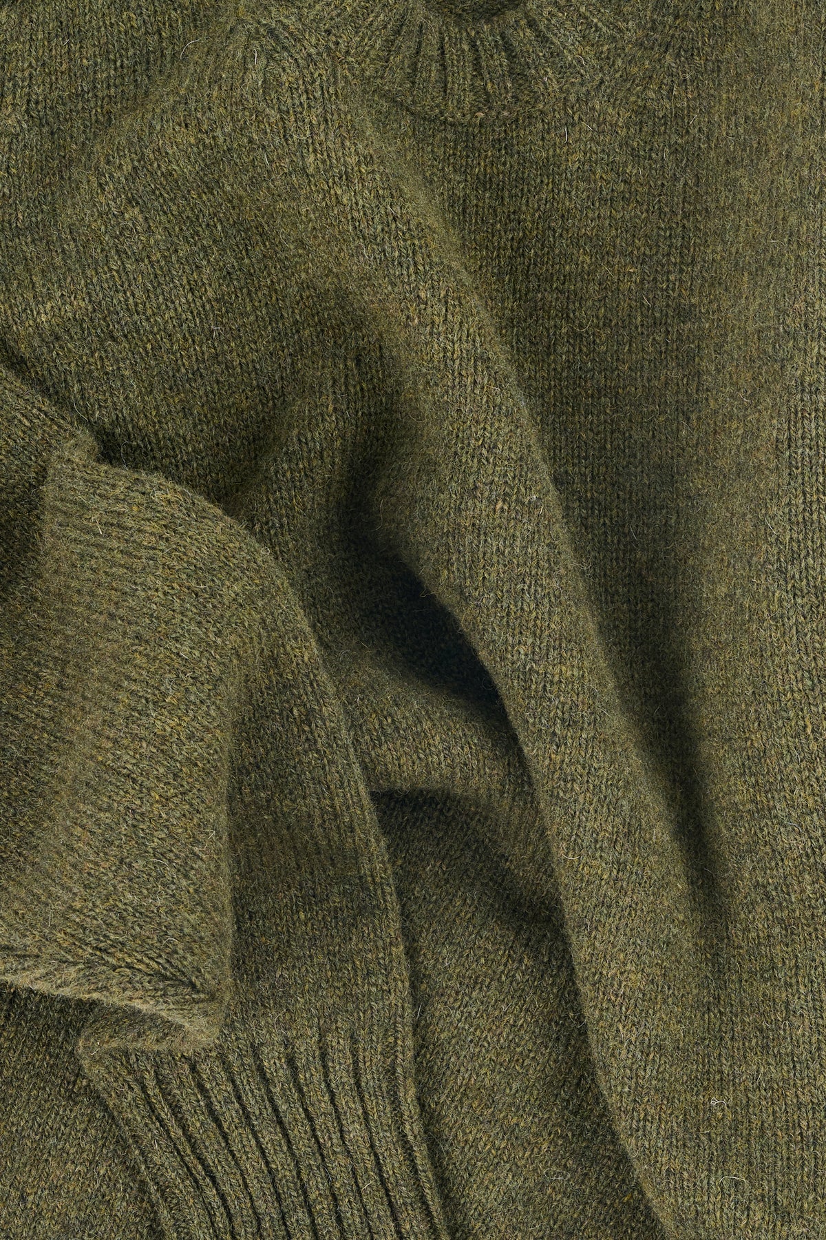 Close up of a green knitted sweater with rib hem and cuff details
