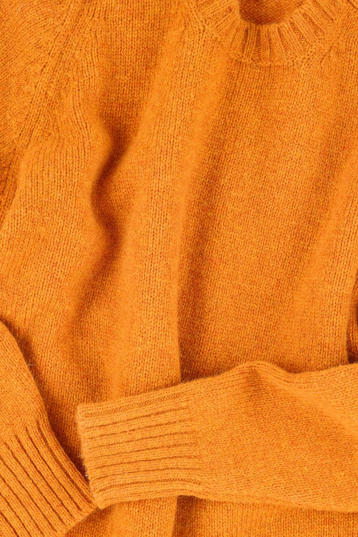 Close up of a knitted orange sweater with ribbed neck, hem and cuff.