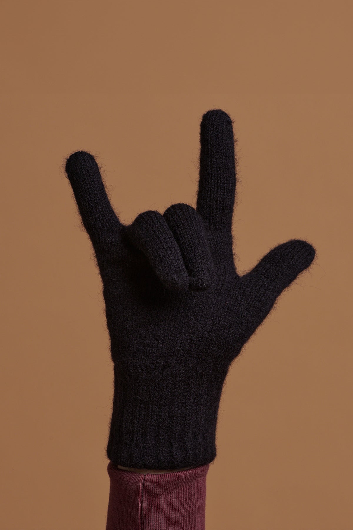 Hand wearing navy lambswool gloves holding the 'hand horns' or rock hand gesture symbol