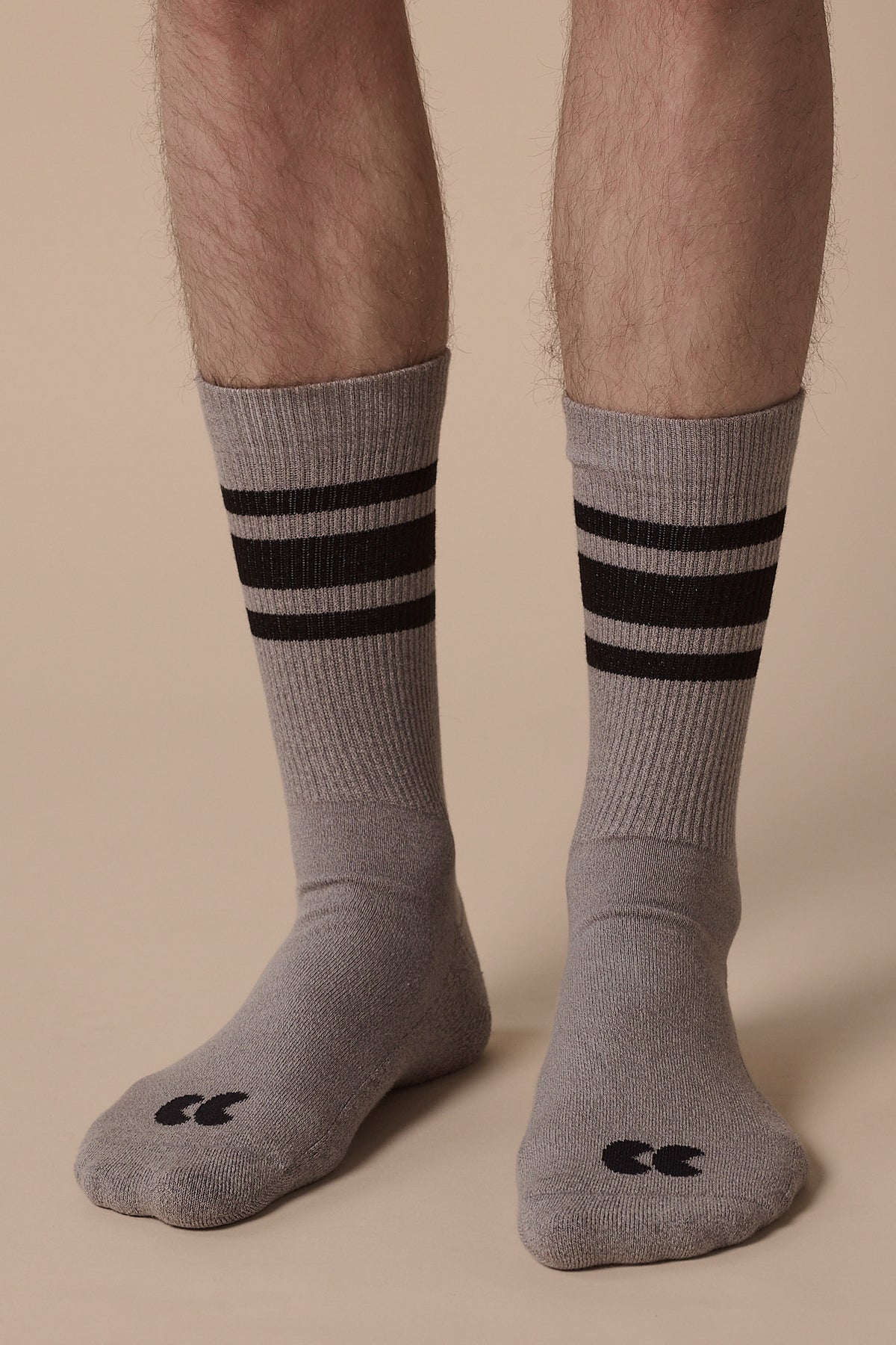 Image of below the knee of model wearing sports cotton sock calf length in grey with black stripes, and CC logo in black on the toe