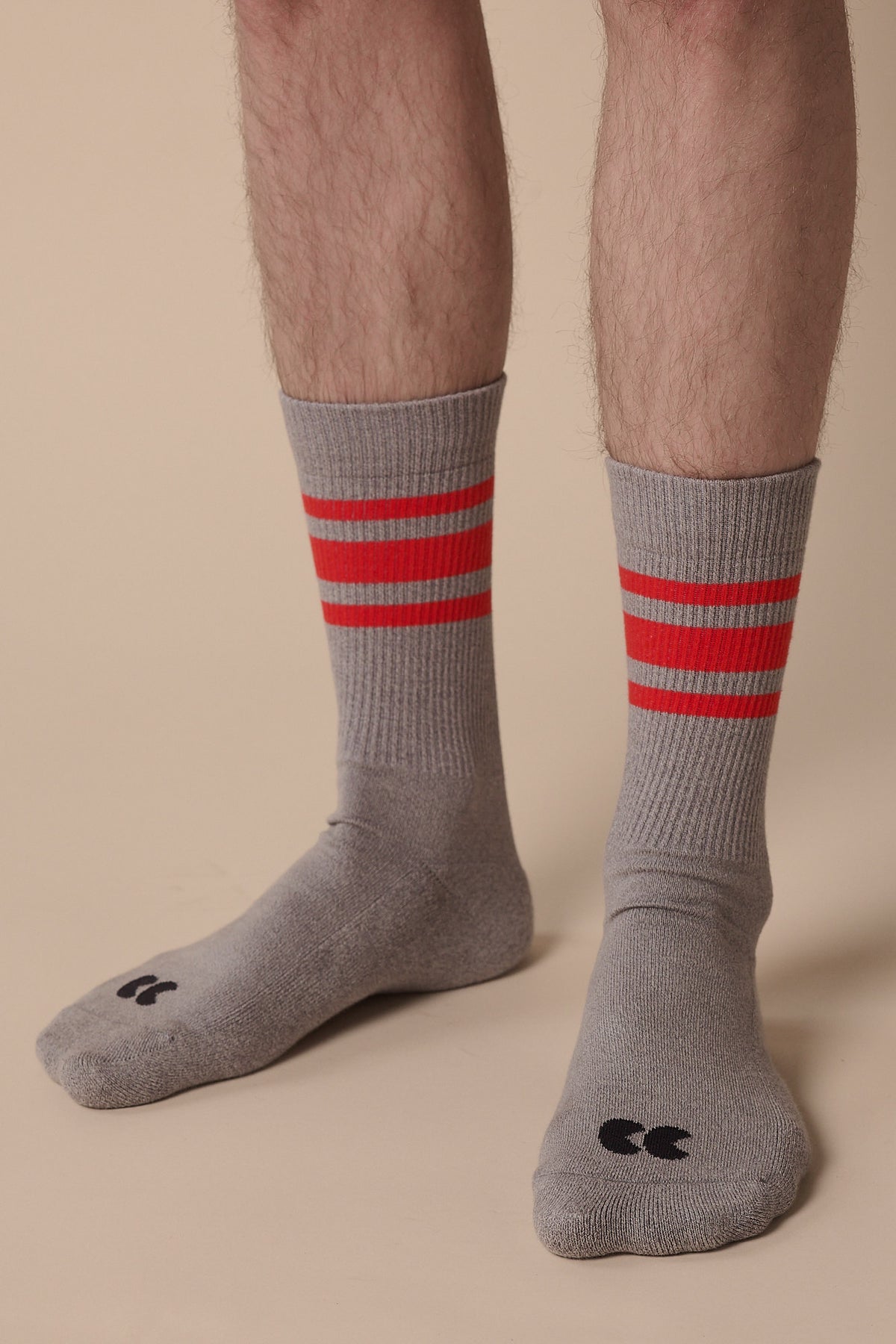 Image of below the knee of model wearing sports cotton sock calf length in grey with red stripes, and CC logo in black on the toe