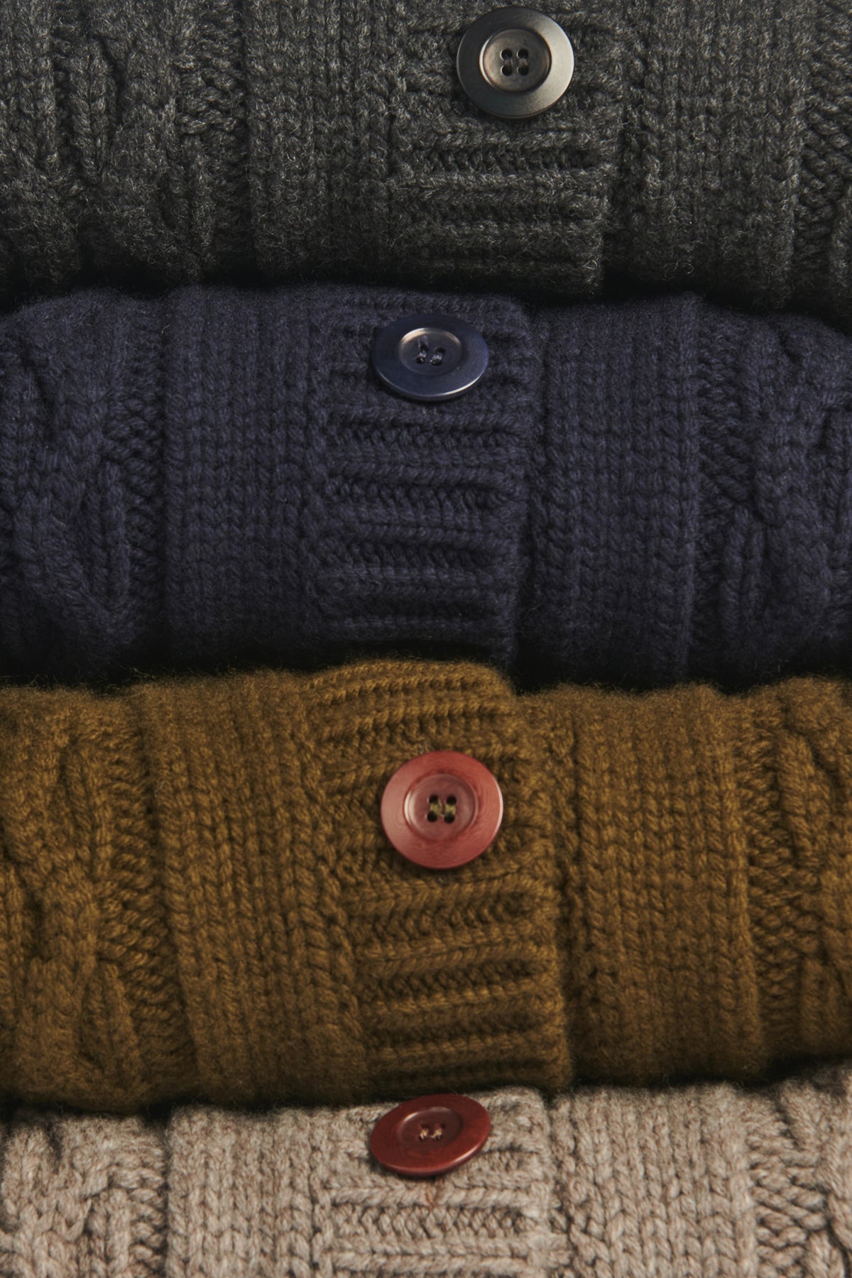 Stack of knitted sweaters in various colors with button details.