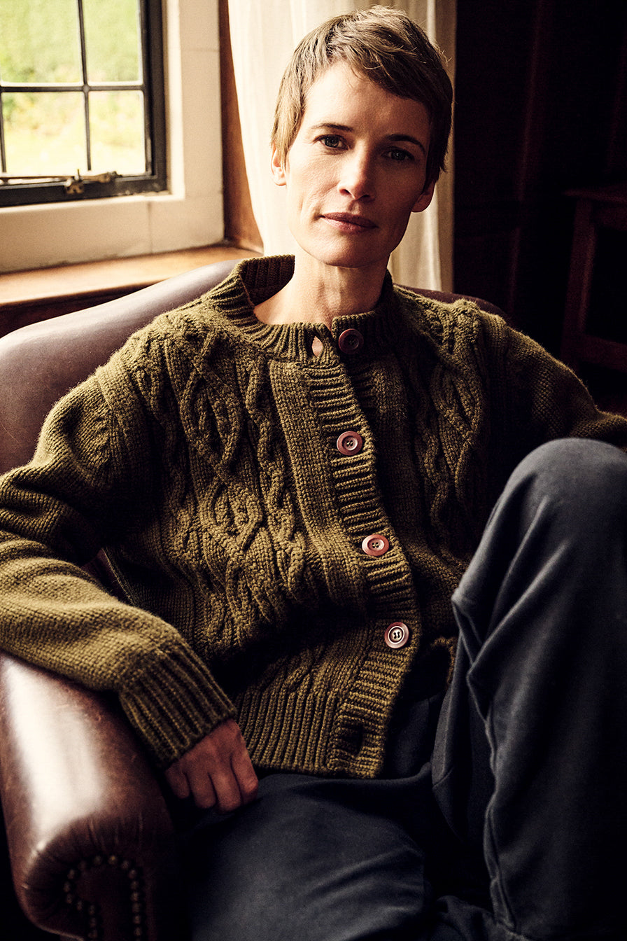 woman sat down on sofa wearing cable knit olive green cardigan