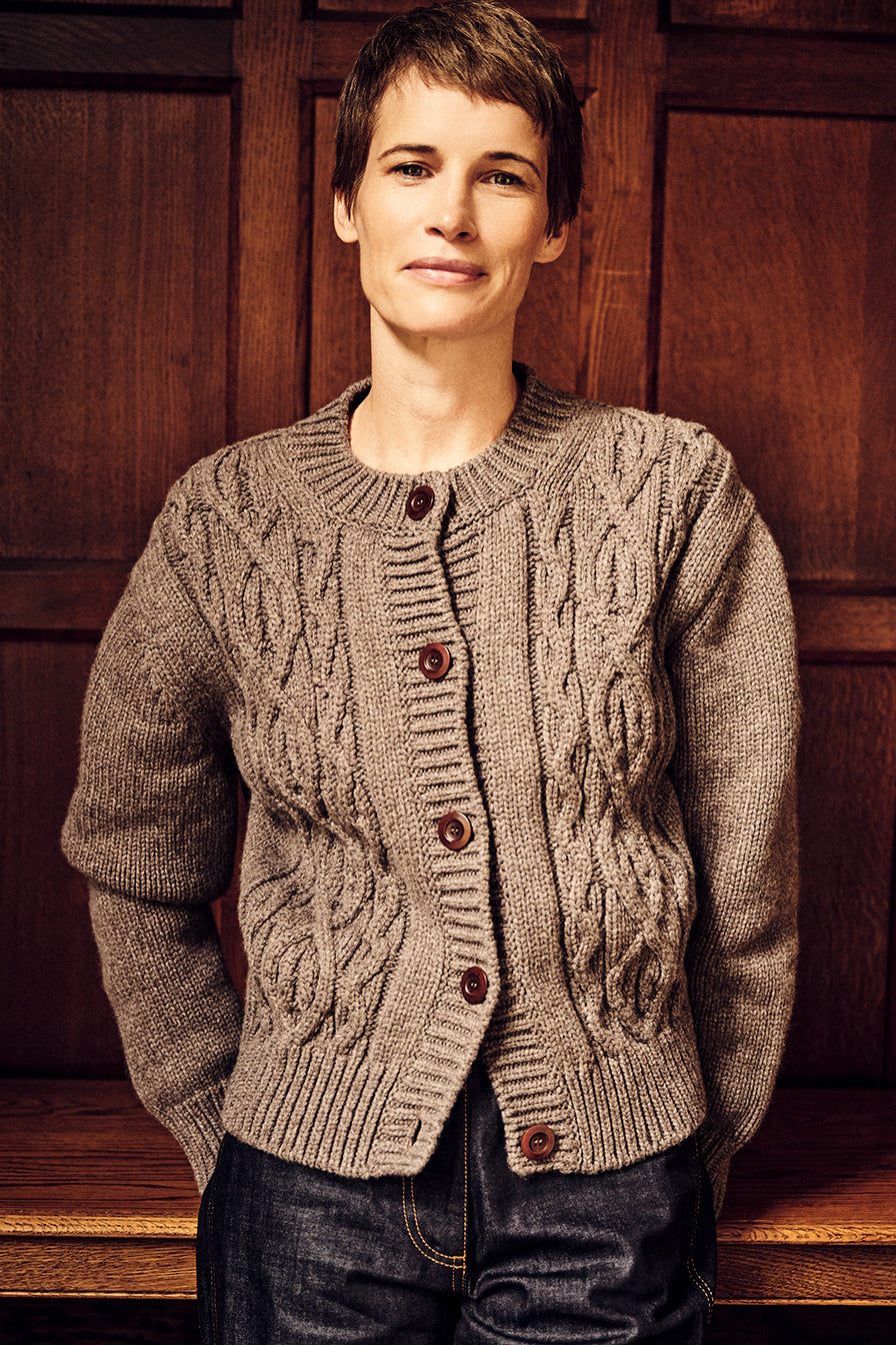 Person wearing a cable knit cardigan against a wooden paneled wall